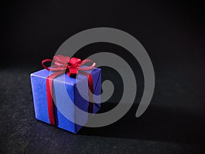 A purple gift box with red ribbon on black background. close up.