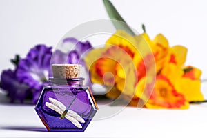 Purple Glass  Bottles with Vintage cork lid and dragonfly picture on white background with blurred purple and yellow flowers.
