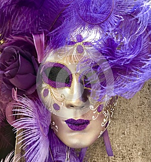 Purple and gold venetian masquerade mask hanging on a wall