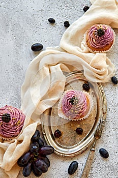 Purple golden cupcake with blackberry on vintage tray decorated with fork, light cloth, fresh blue grapes and blackberries
