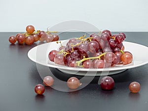 Purple grapes on white plate on the black table