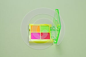 Purple, green, orange and blue eye shadow palette on a green background. Make up. Neon colours