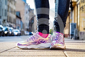 Purple holographic sneakers on a girl legs, with city in the background, selective focus