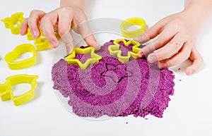 Purple kinetic sand, plastic molds for sand. Child sculpts and plays with sand. Close-up view. White background