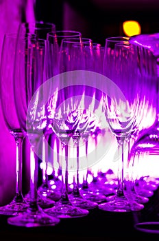 Purple light reflected in the rows of empty clean glasses on the bar counter. Interior of pub or bar at night