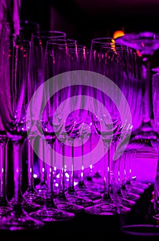 Purple light reflected in the rows of empty clean glasses on the bar counter. Interior of pub or bar at night