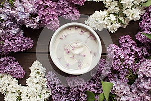 Purple lilac flower sugar in white bowl on dark wooden background with bunch of fresh flowers,