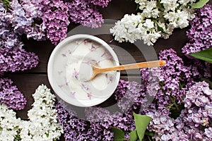 Purple lilac flower sugar in white bowl on dark wooden background with bunch of fresh flowers,