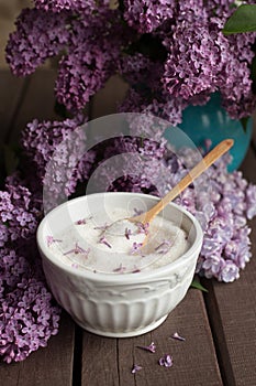 Purple lilac flower sugar in white bowl on dark wooden background with bunch of fresh flowers,