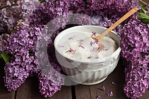 Purple lilac flower sugar in white bowl on dark wooden background with bunch of fresh flowers,