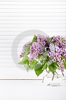 Purple lilac flowers in glass vase on white shutters
