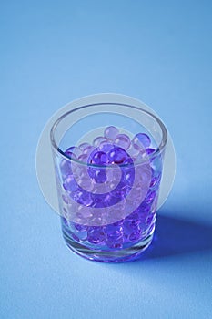 Purple marbles in drinking transparent glass blue background angle view