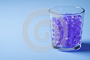 Purple marbles in drinking transparent glass blue background angle view