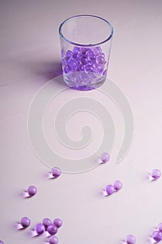 Purple marbles in drinking transparent glass with scattered marbles on white background