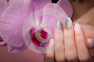 Purple neat manicure on female hands on flowers background. Nail design