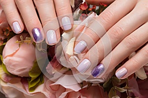 Purple neat manicure on female hands on flowers background. Nail design