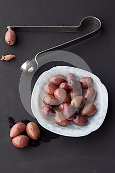 Purple olives in small white bowl with three on black chalk boar