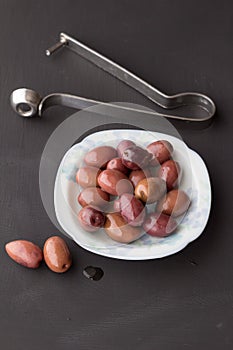 Purple olives in small white bowl with two on black chalk board and stainless steel olive pitter in background