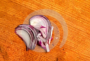 Purple onion thinly sliced on a wooden board. Top view of juicy onion slices