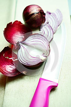 Purple onions and a kitchen knife lie on a lain towel