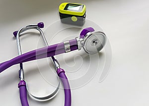 Purple phonendoscope and portable pulse oximeter on white background