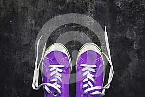 purple-pink-lilac sneakers with untied laces on a dark concrete background. Copy space. View from above