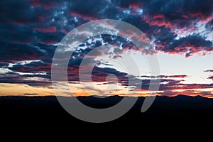 Purple and pink outlines beautiful clouds at sunset over a mountain range silhouetted against the sky