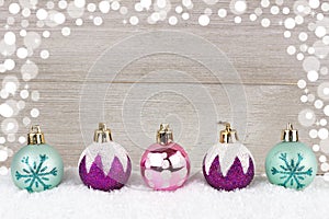 Purple, pink and turquoise Christmas baubles in snow against wood