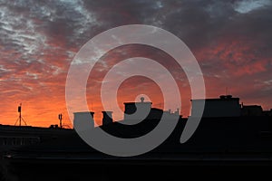 Purple, red and orange sky with dramatc clouds during sunset over the roof, chimneys and antennas of a building in a city urban la