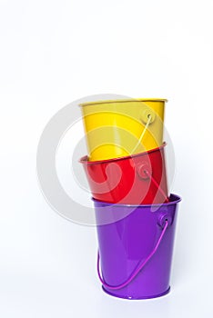 Purple, red, and yellow metal pails stacked together solid white background