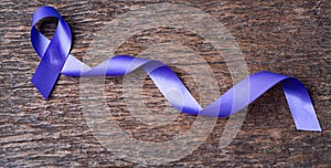 Purple ribbon for the awareness about the unacceptability of the violence against women on dark gray rustic wooden surface. Top