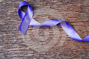 Purple ribbon for the awareness about the unacceptability of the violence against women on dark gray rustic wooden surface. Top