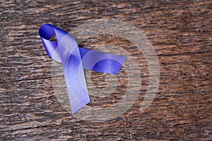 Purple ribbon for the awareness about the unacceptability of the violence against women on dark gray rustic wooden surface. Top