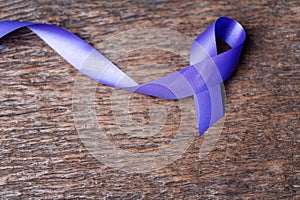 Purple ribbon for the awareness about the unacceptability of the violence against women on dark gray rustic wooden surface. Top