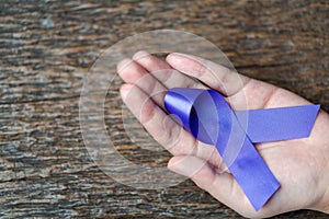 Purple ribbon for the awareness about the unacceptability of the violence against women on dark gray rustic wooden surface. Top