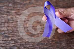 Purple ribbon for the awareness about the unacceptability of the violence against women on dark gray rustic wooden surface. Top