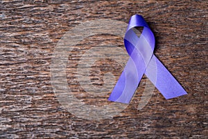 Purple ribbon for the awareness about the unacceptability of the violence against women on dark gray rustic wooden surface. Top