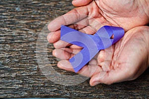 Purple ribbon for the awareness about the unacceptability of the violence against women on dark gray rustic wooden surface. Top