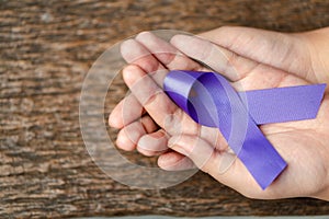 Purple ribbon for the awareness about the unacceptability of the violence against women on dark gray rustic wooden surface. Top