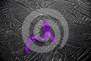 A purple ribbon for the awareness about the unacceptability of the violence against women on a dark gray surface photo