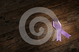 Purple ribbon on brown wooden background. Domestic violence awareness