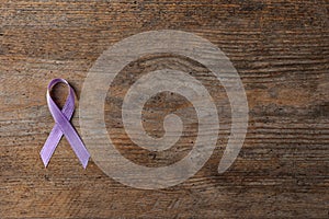 Purple ribbon on brown wooden background, top view. Domestic violence awareness