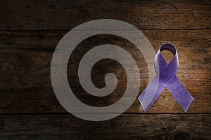 Purple ribbon on brown wooden background, top view. Domestic violence awareness