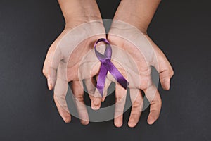 Purple ribbon on cramps hand against black background.