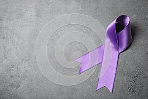 Purple ribbon on grey stone background. Domestic violence awareness