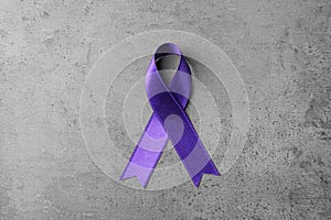 Purple ribbon on grey stone background. Domestic violence awareness