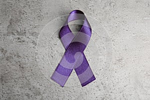 Purple ribbon on grey stone background. Domestic violence awareness