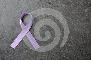 Purple ribbon on grey stone background, top view. Domestic violence awareness