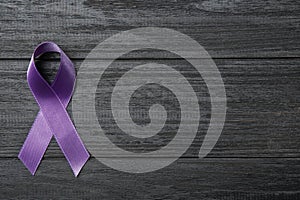 Purple ribbon on grey wooden background, space for text. Domestic violence awareness