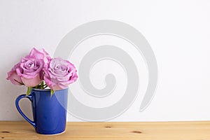 Purple rose flowers in ceramic cup on wooden table with white background